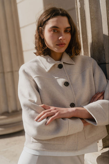 Woman wearing a light-colored coat standing against a neutral background