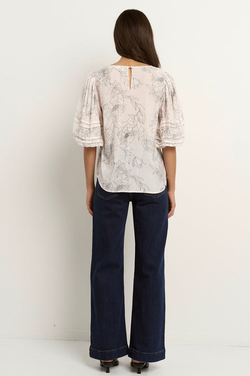 Woman wearing an ivory floral V-neck blouse with ruched puff sleeves, styled with dark indigo denim.