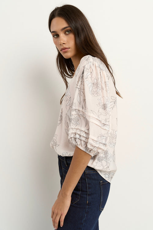 Woman wearing an ivory floral V-neck blouse with ruched puff sleeves, styled with dark indigo denim.