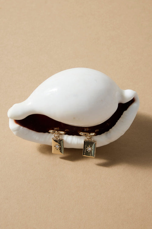 White shell jewelry box with gold charms on a beige background