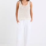 Woman wearing white linen wide leg pants with an elastic waistband, paired with a cream knit tank and sandals, standing against a white background.