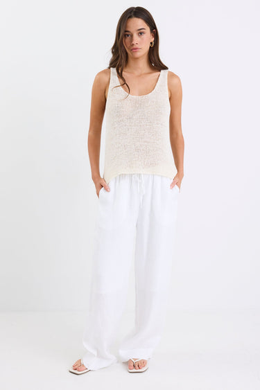 Woman wearing white linen wide leg pants with an elastic waistband, paired with a cream knit tank and sandals, standing against a white background.