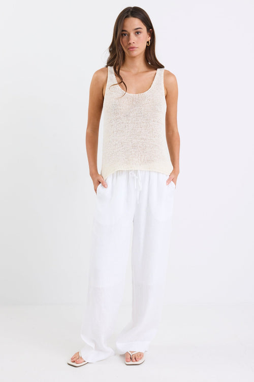 Woman wearing white linen wide leg pants with an elastic waistband, paired with a cream knit tank and sandals, standing against a white background.