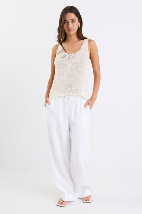 Woman wearing white linen wide leg pants with an elastic waistband, paired with a cream knit tank and sandals, standing against a white background.