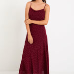 Model wearing a burgundy polka dot strappy maxi dress with a bias-cut silhouette and a flowy skirt