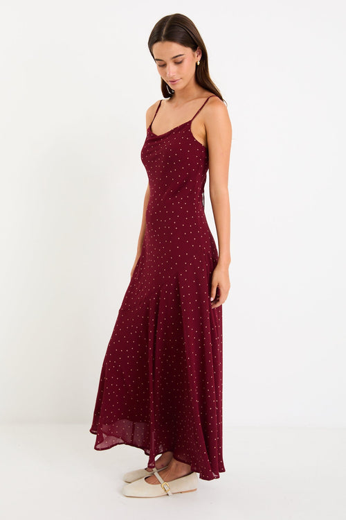 Model wearing a burgundy polka dot strappy maxi dress with a bias-cut silhouette and a flowy skirt