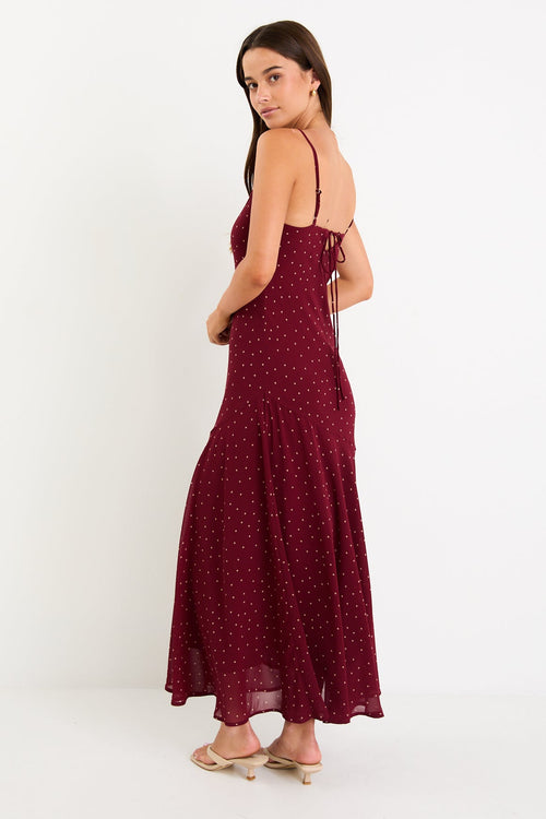 Model wearing a burgundy polka dot strappy maxi dress with a bias-cut silhouette and a flowy skirt