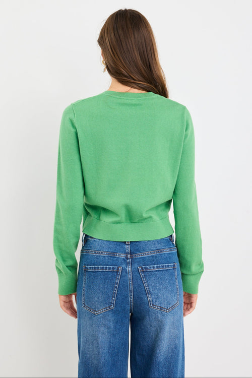 Woman wearing an apple green crewneck cardigan with long sleeves and button-front closure, styled with blue jeans.