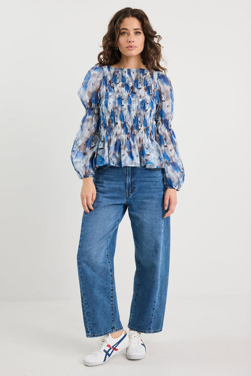 Woman wearing a blue floral blouse and jeans on a white background