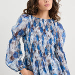 Woman wearing a blue patterned blouse and jeans against a white background