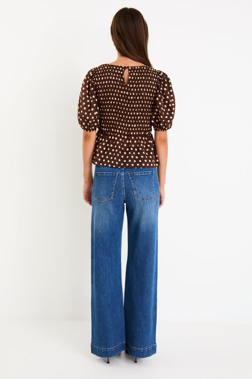 Model wearing a chocolate brown polka dot short sleeve top with a shirred bodice and peplum hem