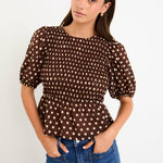 Model wearing a chocolate brown polka dot short sleeve top with a shirred bodice and peplum hem