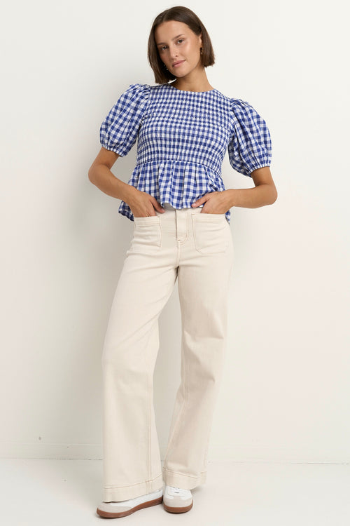 model wears a blue gingham puff sleeve top with ecru jeans