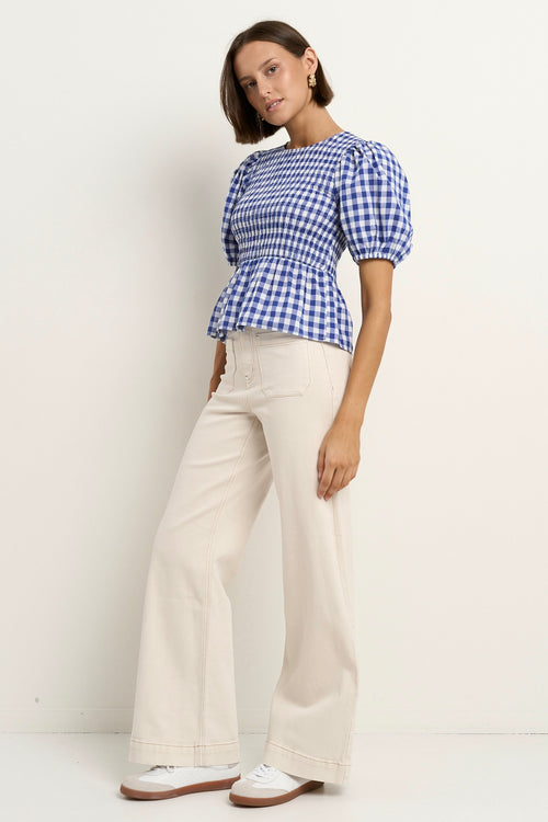 model wears a blue gingham puff sleeve top with ecru jeans