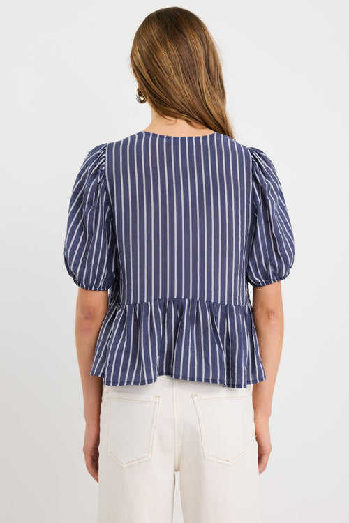 Woman wearing a navy and ivory striped short sleeve peplum top with tie-front closure, styled with ecru jeans.
