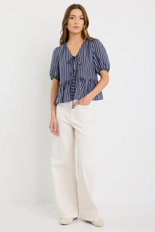 Woman wearing a navy and ivory striped short sleeve peplum top with tie-front closure, styled with ecru jeans.