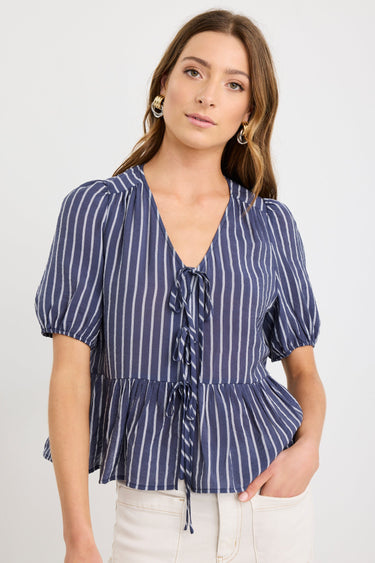 Woman wearing a navy and ivory striped short sleeve peplum top with tie-front closure, styled with ecru jeans.