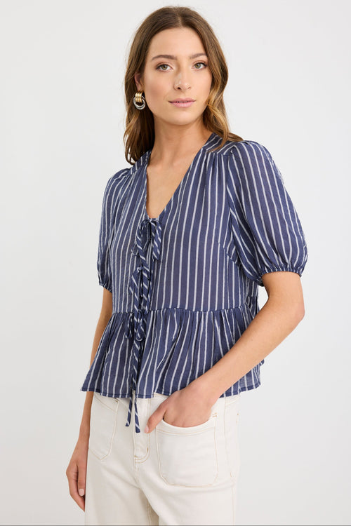 Woman wearing a navy and ivory striped short sleeve peplum top with tie-front closure, styled with ecru jeans.