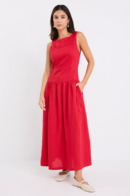 Woman wearing a sleeveless cherry red midi dress with a fitted bodice and gathered skirt, paired with neutral flats.
