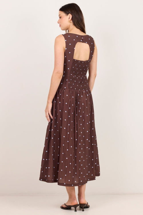 A woman modeling a sleeveless brown midi dress with white polka dots and a cutout back, shown from the rear against a plain light background.