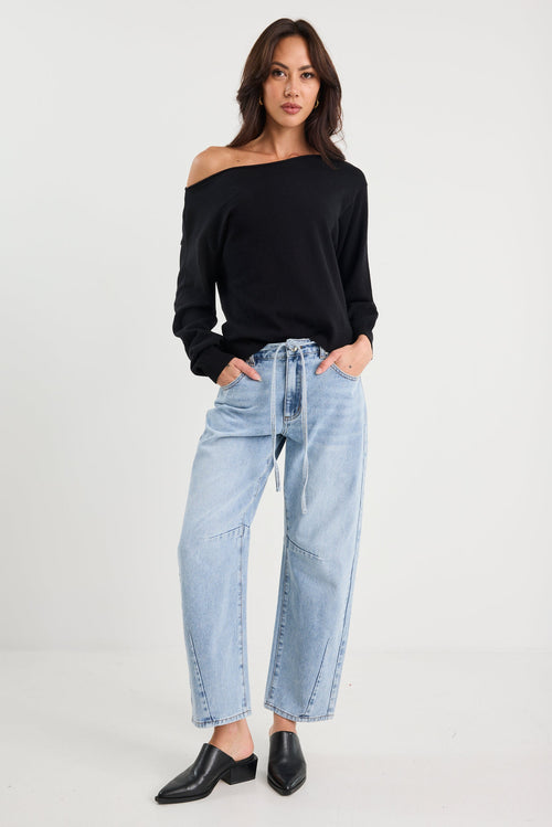 Woman wearing a black off-shoulder top and light blue jeans on a white background