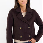 Woman wearing a dark brown peacoat with gold buttons on a white background