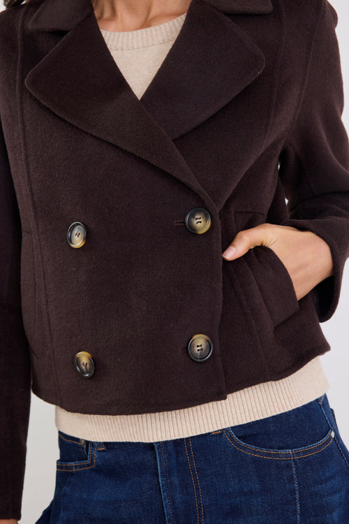 Brown peacoat with gold buttons worn by a person on a white background