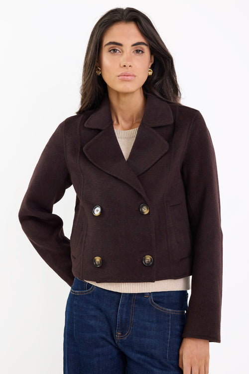 Woman wearing a dark brown jacket with gold buttons on a white background
