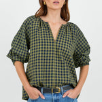 Woman wearing a green and black checkered blouse with blue jeans on a white background
