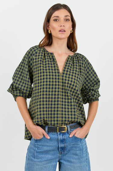 Woman wearing a green and black checkered blouse with blue jeans on a white background