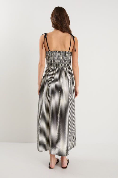 A model wears a black and cream striped maxi dress with strappy sleeves tied at the shoulders and a shirred bodice.