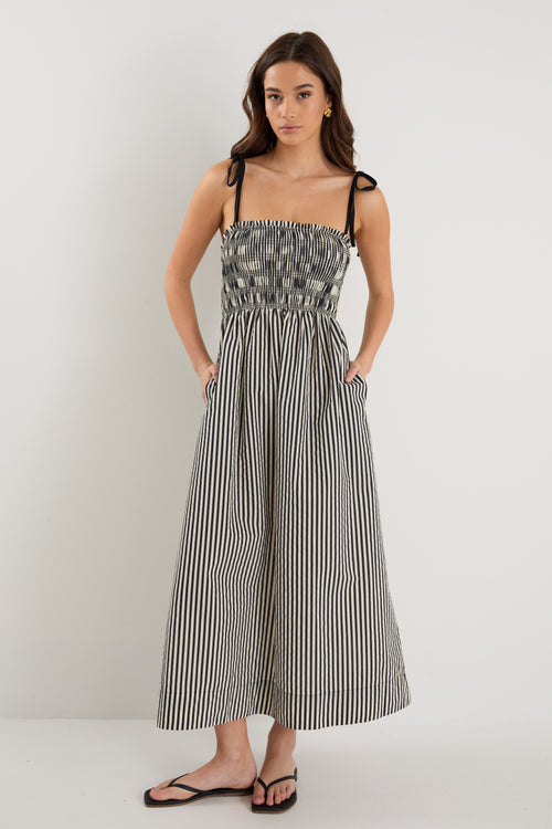 A model wears a black and cream striped maxi dress with strappy sleeves tied at the shoulders and a shirred bodice.