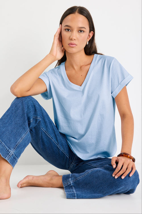 Woman wearing a light blue t-shirt and blue jeans sitting on a white background