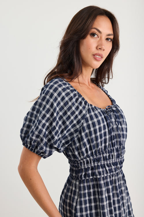 Woman wearing a blue and white checkered dress against a plain background
