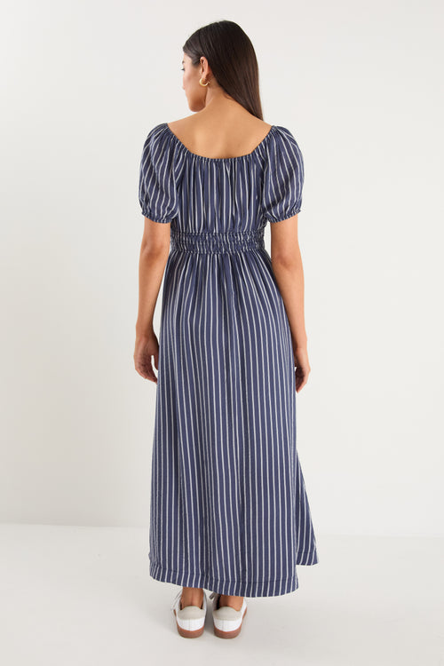 Woman wearing a navy maxi dress with vertical white stripes, short puff sleeves, a smocked waist, and side slit detail.