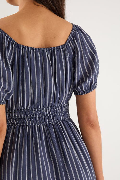 Woman wearing a navy maxi dress with vertical white stripes, short puff sleeves, a smocked waist, and side slit detail.