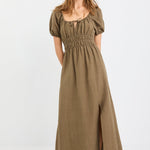 Woman wearing a khaki short sleeve linen blend midi dress with a shirred waist, tie neckline, and side split, styled with white sneakers.
col_pattern