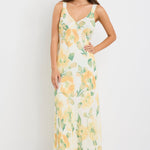 Woman wearing a strappy maxi dress with a honey-yellow floral print on a soft crinkle-textured fabric, cut on the bias for a floaty and elegant silhouette.