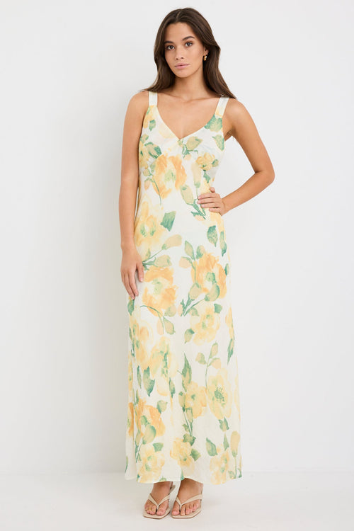 Woman wearing a strappy maxi dress with a honey-yellow floral print on a soft crinkle-textured fabric, cut on the bias for a floaty and elegant silhouette.