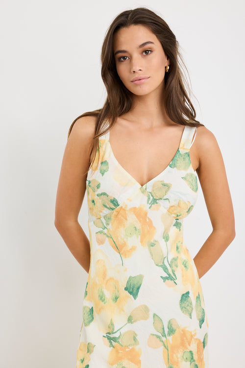 Woman wearing a strappy maxi dress with a honey-yellow floral print on a soft crinkle-textured fabric, cut on the bias for a floaty and elegant silhouette.