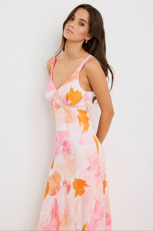 Woman wearing a strappy maxi dress with an abstract pink and orange sunset print, cut on the bias for a floaty and feminine silhouette.