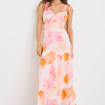 Woman wearing a strappy maxi dress with an abstract pink and orange sunset print, cut on the bias for a floaty and feminine silhouette.