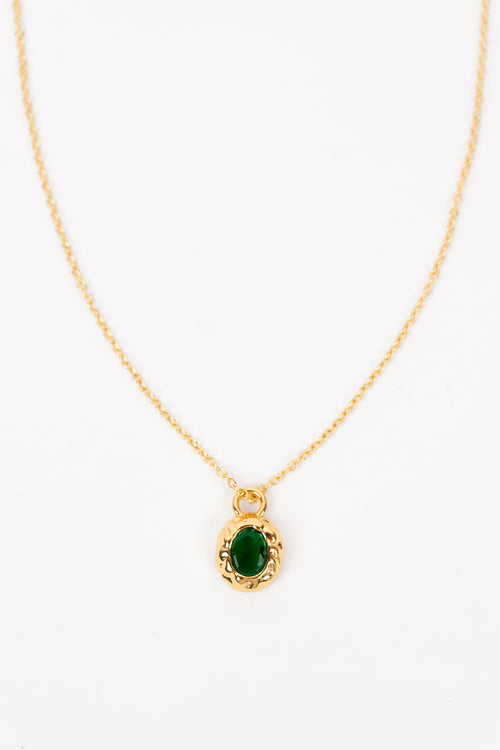 A delicate gold chain necklace featuring an oval pendant with a vibrant green stone surrounded by a textured gold border, set against a plain white background.