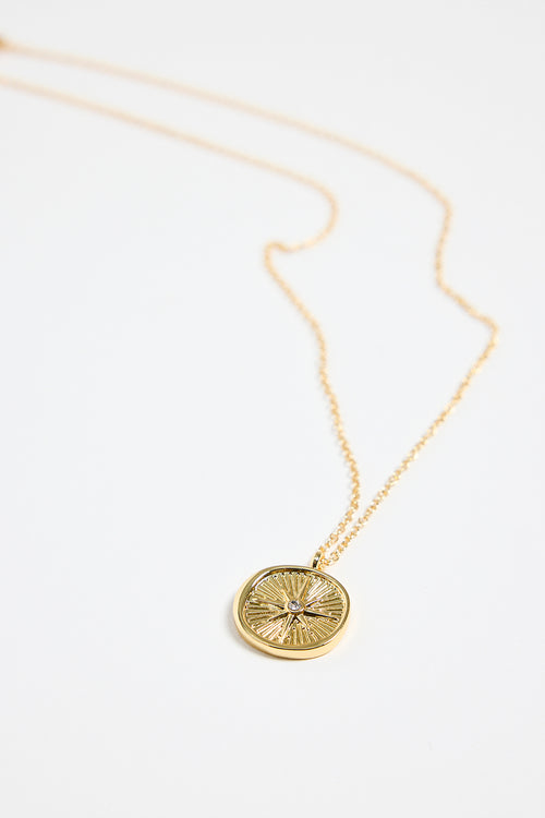gold-plated necklace with fine chain and a round sunburst pendant featuring a central gem detail,