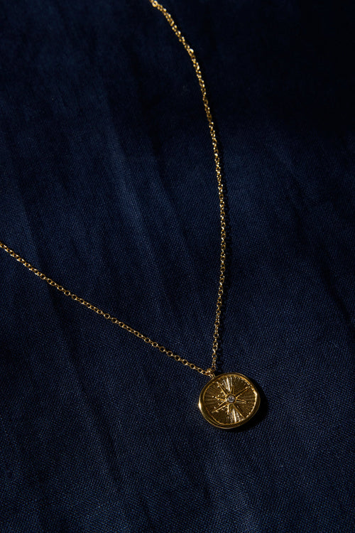 Gold necklace with a round pendant on a dark blue fabric background