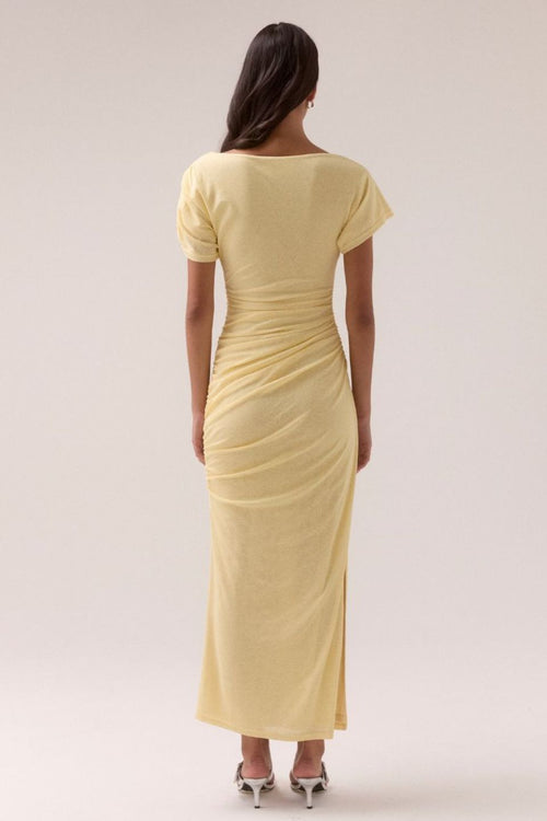 Lemon yellow maxi dress with short sleeves, ruched side detailing, high side slit, and a straight neckline, worn by a model in silver heels against a neutral background.