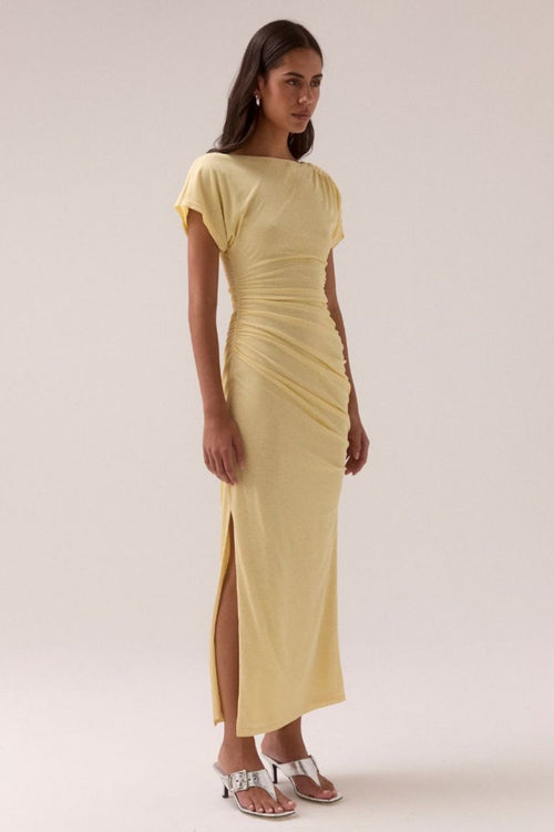 Lemon yellow maxi dress with short sleeves, ruched side detailing, high side slit, and a straight neckline, worn by a model in silver heels against a neutral background.