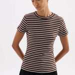 A woman wearing a fitted short-sleeve crewneck top with thin horizontal brown and white stripes, paired with black pants, photographed against a light gray studio background.