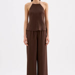 A woman modeling a dark brown two-piece outfit consisting of a halter-neck top and matching wide-leg pants, photographed against a plain light gray studio background.