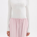 A model wearing a white long-sleeve mock neck top and light pink drawstring lounge pants against a plain white background.